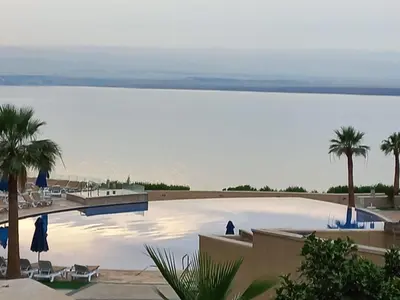 a large swimming pool with palm trees and a body of water at Sunset apartment in Samarah Dead Sea resort in Sowayma