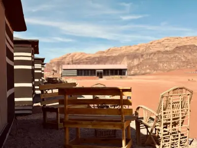 a wooden bench and chairs sitting in the desert at Salameh's Bedouin Camp in Wadi Rum