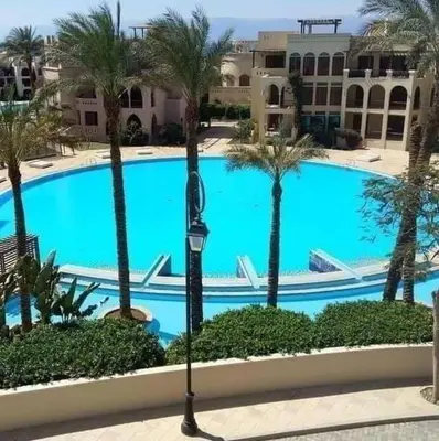 a large pool with palm trees in front of a building at Lovely first floor tow bed rooms overviewing circular pool for families only in Talabay Aqaba in Aqaba