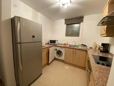 a kitchen with a refrigerator and a washing machine at Lovely first floor tow bed rooms overviewing circular pool for families only in Talabay Aqaba in Aqaba