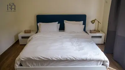a bed with a blue headboard and white sheets and pillows at Maison Gaia, A Stylish Apartment in the heart of Amman in Amman