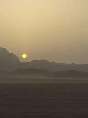 a sunset in the desert with mountains in the background at Enjoy Wadi Rum stars in Disah