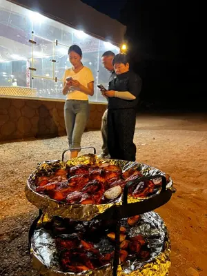 a group of people standing around a grill with food at Jori Luxury Camp in Wadi Rum