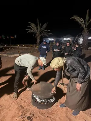 a group of people standing around a pot in the sand at Desert Nights Camp in Wadi Rum