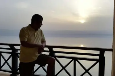 a man sitting on a fence near the ocean at Dead Sea Jordan Sea View Samarah Resort Traveler Award 2024 winner in Sowayma