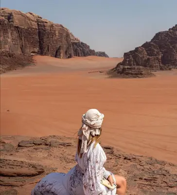 a woman sitting on a rock in the desert at Golden sunset luxury camp in Wadi Rum