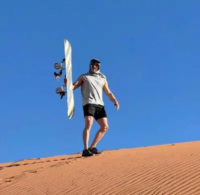 a man standing on a sand dune with a surfboard at Wadi rum Rozana camp in Wadi Rum