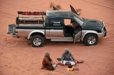 two men sitting in the sand next to a van in the desert at Sami Al Muzna Rum Camp in Wadi Rum