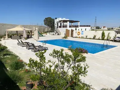 a swimming pool with chairs and umbrellas next to a building at Qaimariya Farmhouse Amman - Day Use - Lodging - Events in Amman
