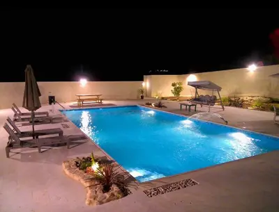 a swimming pool at night with two chairs and a table at Qaimariya Farmhouse Amman - Day Use - Lodging - Events in Amman