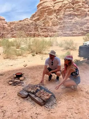 a man and a woman cooking food over a fire at wadi rum tha moon in Wadi Rum