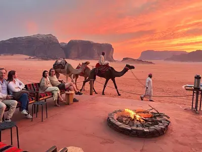a group of people riding camels around a fire in the desert at wadi rum tha moon in Wadi Rum