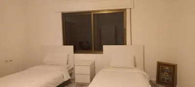 two beds in a white room with a window at Khalda Apartments for females in Amman