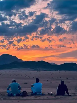 three people sitting on the beach watching the sunset at Wadi Rum Santa Camp in Wadi Rum