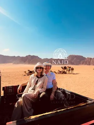 a man and woman sitting in a camel drawn cart in the desert at Najd Luxury Camp in Wadi Rum
