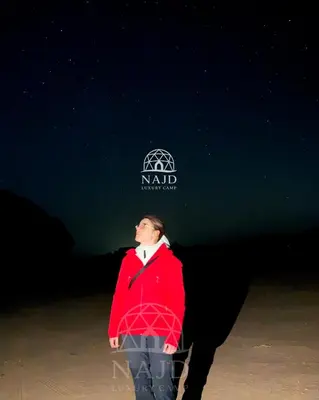 a man in a red jacket standing on the beach at Najd Luxury Camp in Wadi Rum
