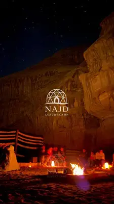 a tent with a fire in front of a rock wall at Najd Luxury Camp in Wadi Rum
