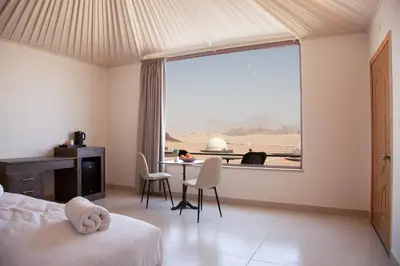 a bedroom with a bed and a table and a large window at Omsiat Shahrazad Luxury Camp in Wadi Rum