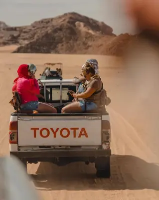 three people sitting in the back of a truck in the desert at Charlotte luxury camp in Wadi Rum
