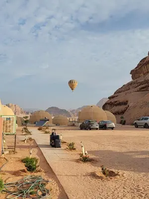 a hot air balloon flying over a desert with cars at MAXIMAS LUXURY Wadi Rum in Wadi Rum