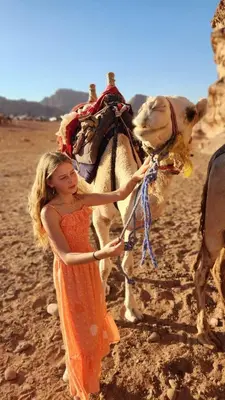 a woman in an orange dress standing next to a camel at Tamim Luxury wadi rum camp in Wadi Rum