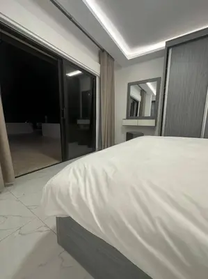 a bedroom with a white bed and a large window at cozy rooftop near al services 23 in Rujm ash Sharāʼirah
