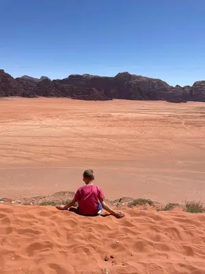a person sitting on the sand in the desert at Wadi Rum Legacy Camp & Tours in Wadi Rum