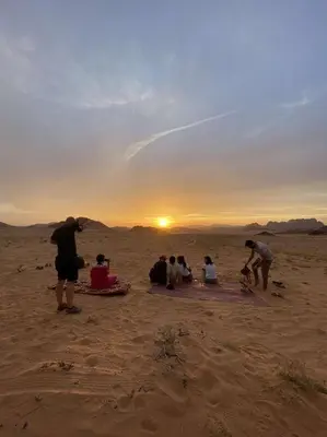 a group of people sitting in the desert watching the sunset at Wadi Rum Legacy Camp & Tours in Wadi Rum