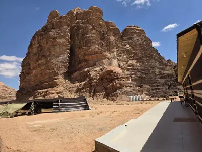 a large rocky mountain in the desert next to a building at Luxury tent camp in Wadi Rum