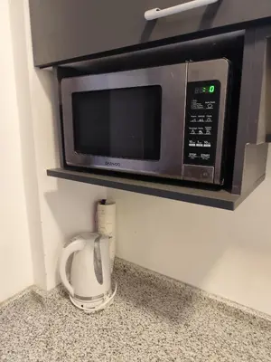a microwave on a shelf above a counter with a coffee cup at Gentle Breeze Studio 1 in Amman