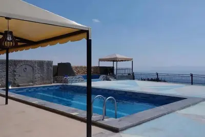 a swimming pool with an umbrella next to the ocean at Magical Rosemary Chalet in Al Mashāriqah
