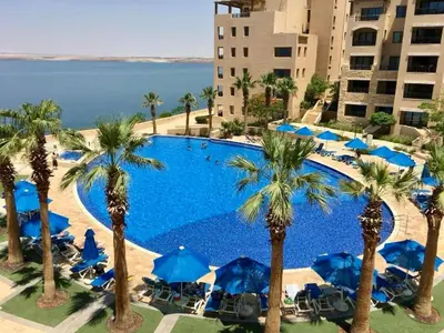 a large swimming pool with palm trees and blue umbrellas at E21 Samarah Resort Apartments in Sowayma