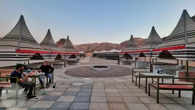 two people sitting at tables in a courtyard with mountains at Magical desert camp in Disah