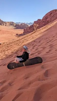 a woman sitting on the sand in the desert at Wadi Rum Magic Stars in Wadi Rum