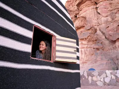 a woman looking out the window of a black and white house at Wadi Rum Backpacker Camp in Wadi Rum