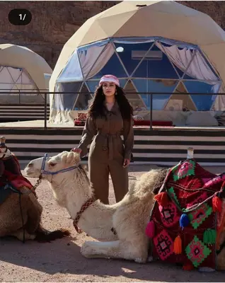 a woman is standing next to a camel at Enjoy Camp Bubble Luxury with Jeep Tour in Wadi Rum