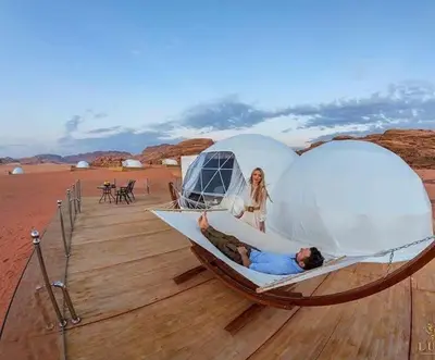 a man and woman laying in a hammock in a tent at Enjoy Camp Bubble Luxury with Jeep Tour in Wadi Rum