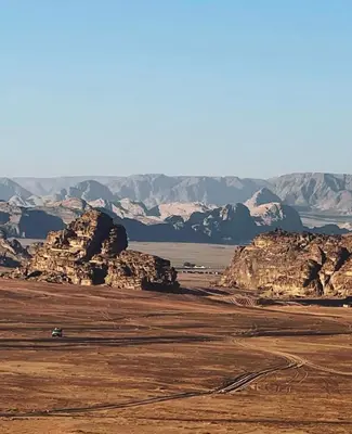 a truck driving through a desert with mountains in the background at Khaled Rum Camp in Disah