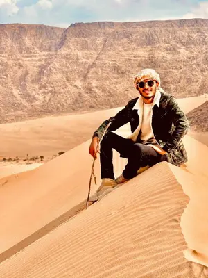 a man sitting on a sand dune in the desert at Khaled Rum Camp in Disah