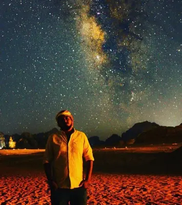 a man standing on a beach under a starry sky at Moon City Luxury Tent in Wadi Rum