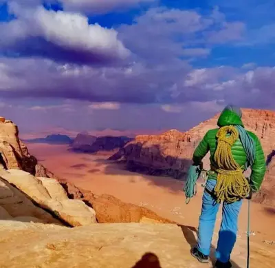 a man with a backpack standing on top of a mountain at Moon City Luxury Tent in Wadi Rum
