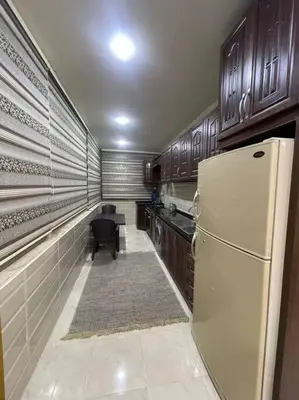 a kitchen with a white refrigerator and wooden cabinets at شقة مفروشة in Rujm Maghghijhah