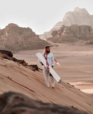 a man walking in the desert holding a surfboard at Romantic Moment Rum CAMP in Wadi Rum