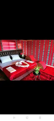 a bedroom with two beds with red sheets and a table at Rum Honeymoon Camp in Wadi Rum