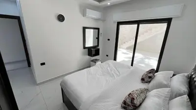 a white bedroom with a bed and a window at شقة بثلاث غرف نوم الجاردنز عمو سامي in Amman