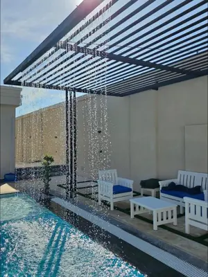 a swimming pool with two white benches and a water fountain at Tixos Farm in Irbid