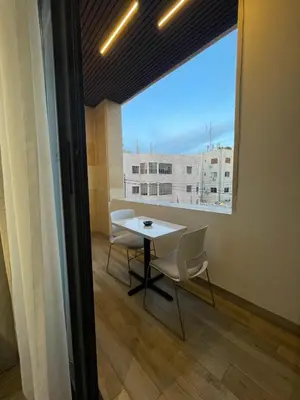 a table and chairs in a room with a large window at Soho Midtown in Ash Shumaysānī