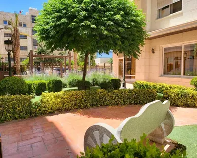 a park bench in front of a tree and a building at Residents Specialists in Amman