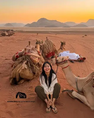 a woman kneeling next to a group of camels in the desert at ROYAL MOON BUBBLES lUXURY CAMP in Wadi Rum