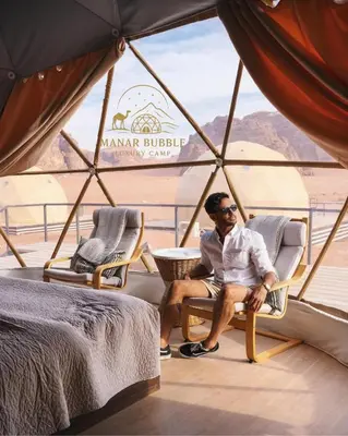 a man sitting in a chair in front of a window at Manar Bubbel Luxury Camp in Wadi Rum